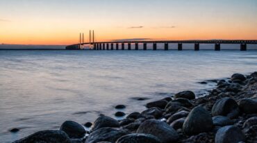 Öresundsbron i skymning sedd från strandkanten med vatten i förgrunden