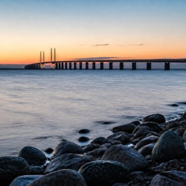 Öresundsbron i skymning sedd från strandkanten med vatten i förgrunden