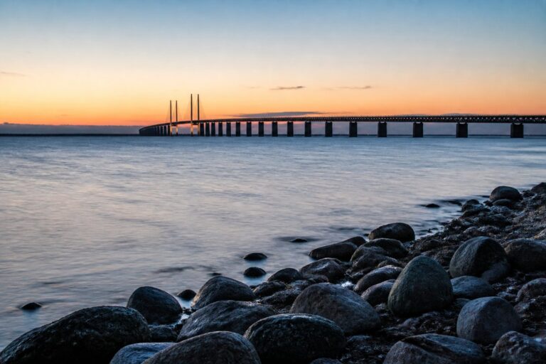 Öresundsbron i skymning sedd från strandkanten med vatten i förgrunden